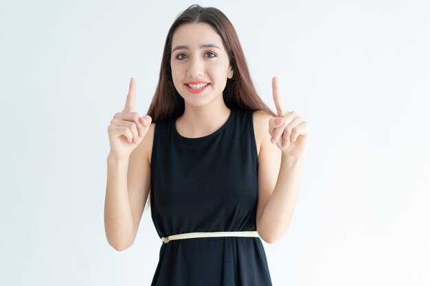 Retrato de mujer asiática joven feliz apuntando hacia arriba y sonriendo