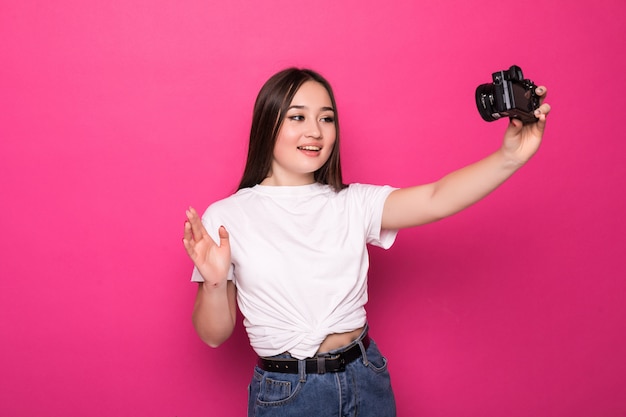 Retrato de una mujer asiática joven feliz vestida con un vestido blanco y un sombrero de verano con cámara fotográfica y mirando a otro lado en el espacio de la copia sobre la pared rosa