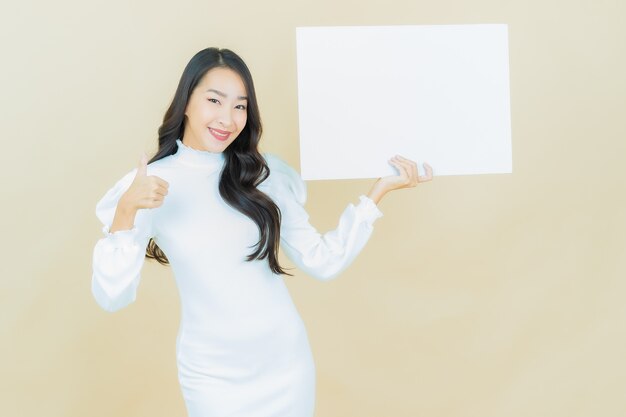 Retrato de mujer asiática joven hermosa con cartelera blanca vacía en la pared de color