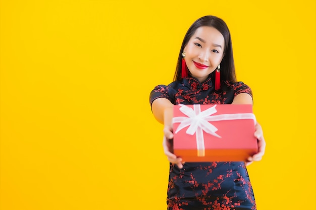 El retrato de la mujer asiática joven hermosa viste el vestido chino y sostiene la caja de regalo roja