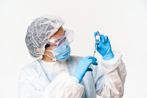 Retrato de mujer asiática médico, enfermera que vacuna a pacientes, con jeringa y vacuna covid-19, de pie en equipo de protección personal, fondo blanco.