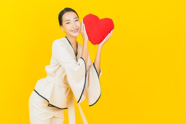 Retrato de mujer asiática de negocios joven hermosa con almohada en forma de corazón en la pared de color amarillo