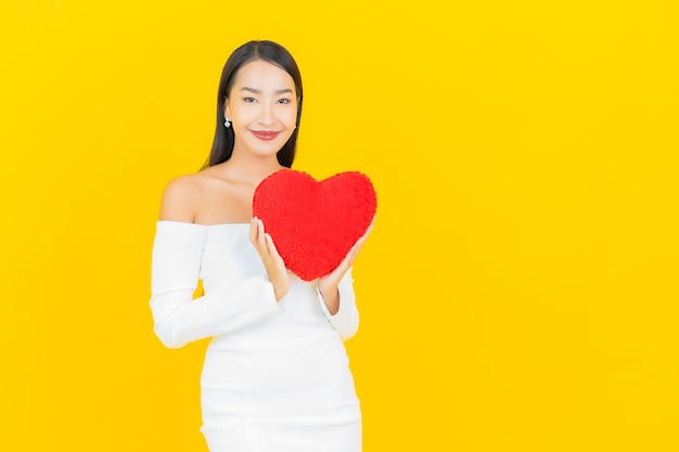 Retrato de mujer asiática de negocios joven hermosa con almohada en forma de corazón en la pared de color amarillo