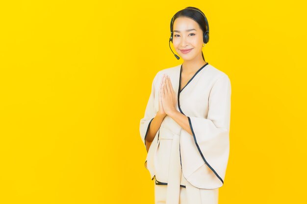 Retrato de mujer asiática de negocios joven hermosa con auriculares para atención al cliente del centro de llamadas en la pared amarilla