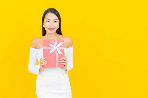 Retrato de mujer asiática de negocios joven hermosa con caja de regalo roja en la pared amarilla