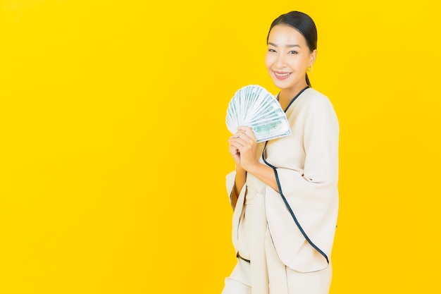 Retrato de mujer asiática de negocios joven hermosa con una gran cantidad de dinero en efectivo y hucha en la pared amarilla