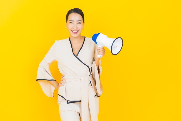 Retrato de mujer asiática de negocios joven hermosa con megáfono para comunicación en pared amarilla