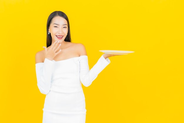 Retrato de mujer asiática de negocios joven hermosa con plato de plato vacío en la pared amarilla