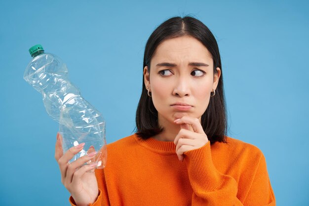 Foto gratuita retrato de una mujer asiática preocupada mirando preocupada una botella de plástico pensando dónde reciclar la b azul