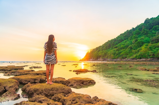 Retrato de mujer asiática en la roca al atardecer alrededor del océano en vacaciones