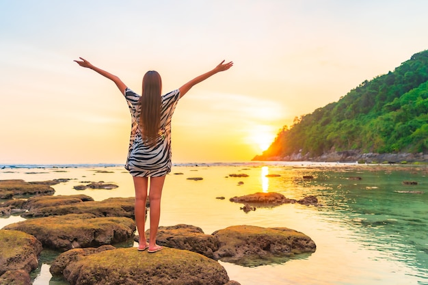 Retrato de mujer asiática en la roca con los brazos abiertos al atardecer alrededor del océano en vacaciones