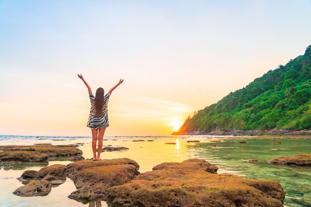 Retrato de mujer asiática en la roca con los brazos abiertos al atardecer alrededor del océano en vacaciones