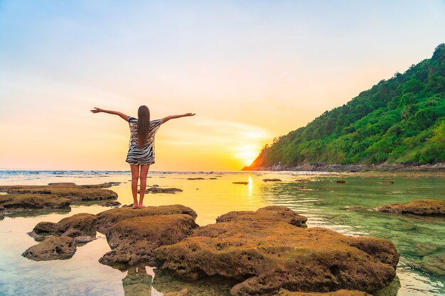 Retrato de mujer asiática en la roca con los brazos abiertos al atardecer alrededor del océano en vacaciones