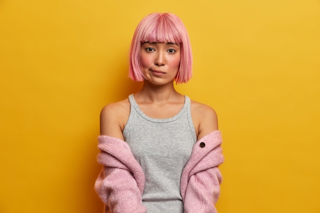 Foto gratuita retrato de mujer asiática seria con cabello rosado, se ve aburrida, frunce los labios, tiene mejillas rojas