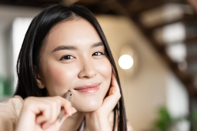 Retrato de mujer asiática sonriente cara que parece feliz sosteniendo la pluma y sonriendo abiertamente trabajando o haciendo los deberes