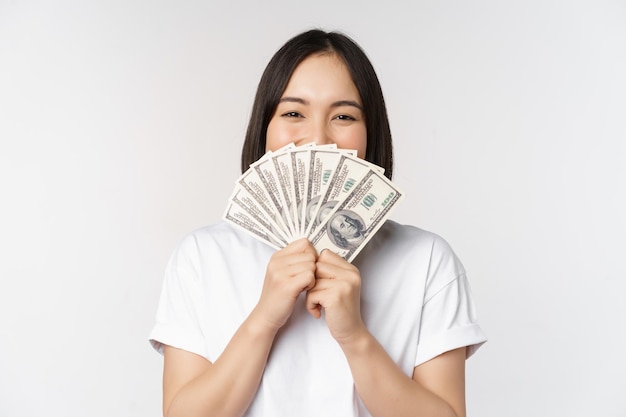 Retrato de una mujer asiática sonriente sosteniendo dólares dinero concepto de financiación de microcréditos y dinero en efectivo de pie sobre fondo blanco.