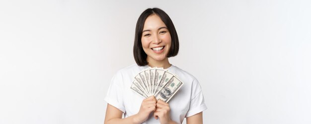 Retrato de una mujer asiática sonriente sosteniendo dólares dinero concepto de financiación de microcréditos y dinero en efectivo de pie sobre fondo blanco.