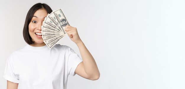 Retrato de una mujer asiática sonriente sosteniendo dólares dinero concepto de financiación de microcréditos y dinero en efectivo de pie sobre fondo blanco.