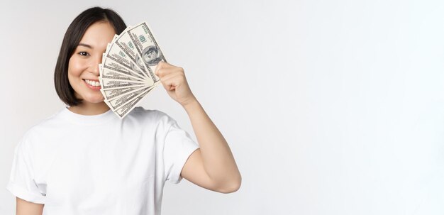 Retrato de una mujer asiática sonriente sosteniendo dólares dinero concepto de financiación de microcréditos y dinero en efectivo de pie sobre fondo blanco.