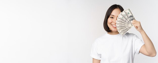 Retrato de una mujer asiática sonriente sosteniendo dólares dinero concepto de financiación de microcréditos y dinero en efectivo de pie sobre fondo blanco.