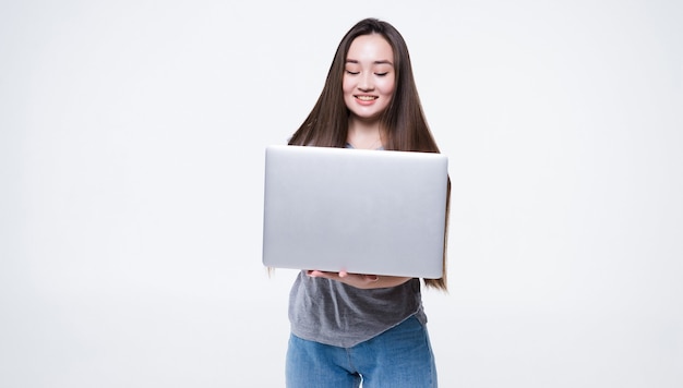 Retrato de una mujer asiática sonriente sosteniendo el ordenador portátil aislado en la pared gris