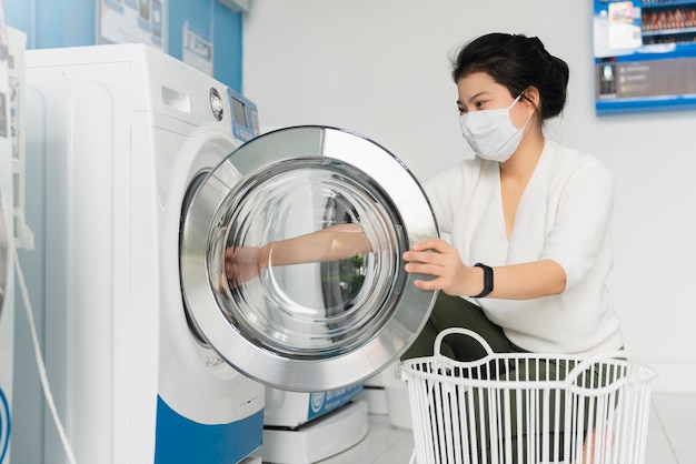 Retrato mujer asiática usa máscara protectora de virus en la propagación de covid19 lavado en color azul lavandería interior en la ciudad de condoiminuim nuevo estilo de vida normal