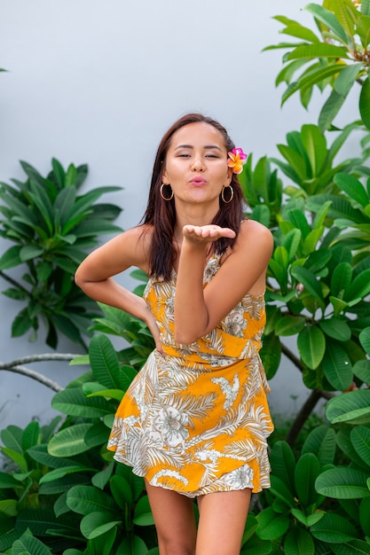 Foto gratuita retrato de mujer asiática en vestido amarillo de verano se encuentra con flor tailandesa plumeria en el pelo y pendientes redondos