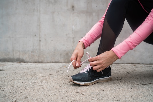 Retrato de una mujer atlética atarse los cordones de sus zapatos y preparándose para correr al aire libre. Concepto de deporte y estilo de vida saludable.