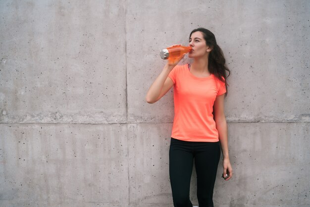 Retrato de una mujer atlética bebiendo agua después del entrenamiento contra un fondo gris. Estilo de vida deportivo y saludable.
