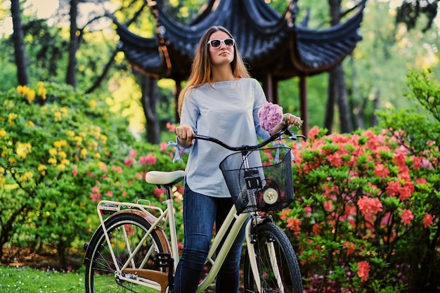 Retrato de mujer atractiva con bicicleta de la ciudad cerca del pabellón chino tradicional en un parque.