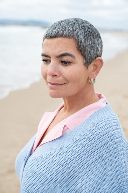 Retrato de mujer atractiva caminando cerca del mar. Modelo femenino con cabello corto caminando en un día nublado. Naturaleza, concepto de tiempo libre