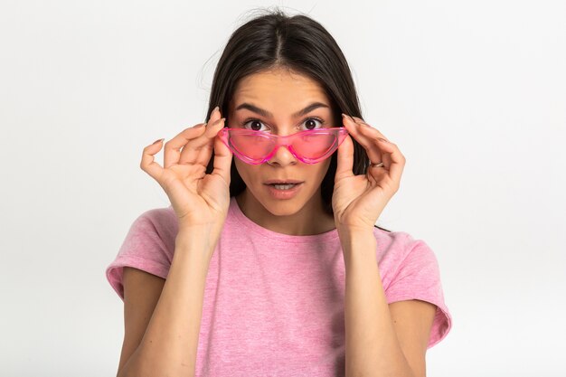 Foto gratuita retrato de mujer atractiva en camiseta rosa con elegantes gafas de sol aislado sorprendido sorprendido expresión de la cara mirando