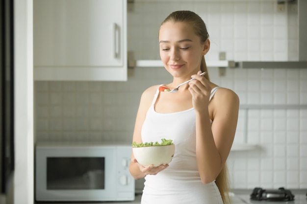 Foto gratuita retrato de mujer atractiva degustación de ensalada fresca en la cocina