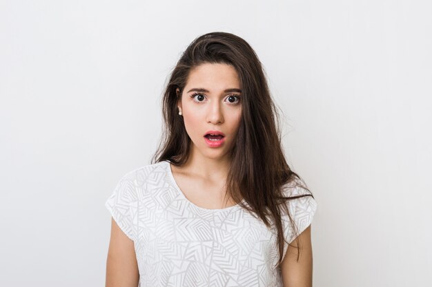 Retrato de mujer atractiva con expresión de asombro de cara, primer plano, ojos abiertos y boca, emocional, aislado