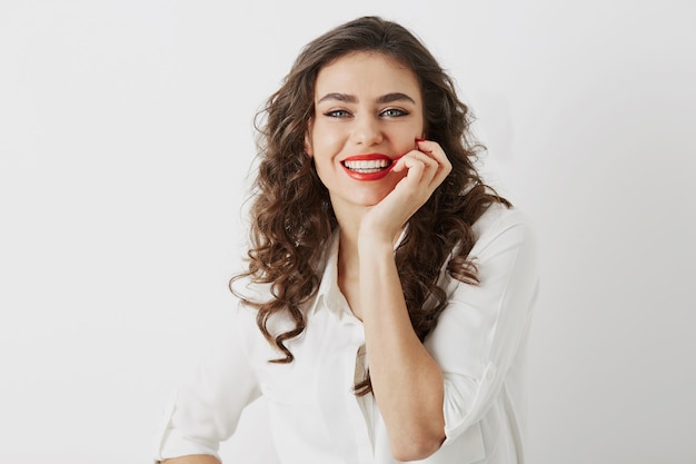 Retrato de mujer atractiva sonriente sincera con dientes blancos aislados, pelo largo y rizado, blusa blanca, estilo de negocios elegante, emoción positiva feliz, maquillaje de lápiz labial rojo de cerca