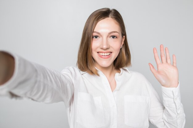 Retrato de mujer atractiva sonriente tomando un selfie mientras está aislado