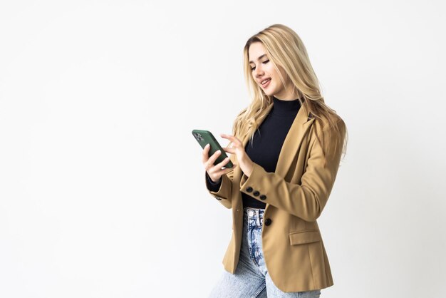 Retrato de una mujer atractiva sorprendida que sostiene el teléfono móvil y que mira la cámara aislada sobre el fondo blanco