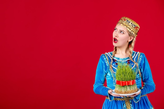 Foto gratuita retrato de mujer azerí en vestido tradicional sosteniendo semeni estudio disparó fondo rojo novruz concepto étnico primavera