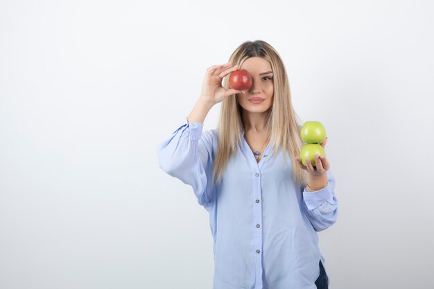 Retrato de una mujer bastante atractiva modelo de pie y cubriendo los ojos con una manzana roja fresca.