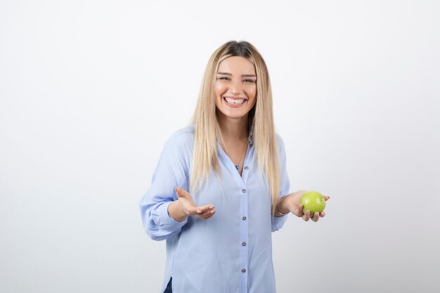 Retrato de una mujer bastante atractiva modelo de pie y sosteniendo una manzana verde fresca.