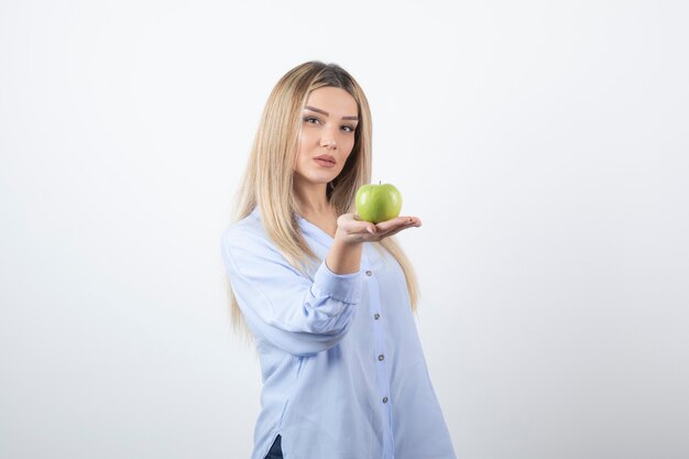 Retrato de una mujer bastante atractiva modelo de pie y sosteniendo una manzana verde fresca.