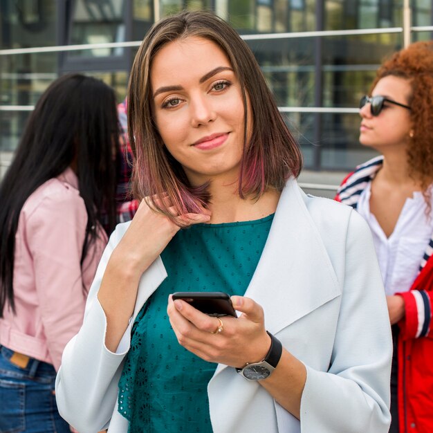 Retrato de una mujer bastante elegante que sostiene el teléfono móvil que mira la cámara