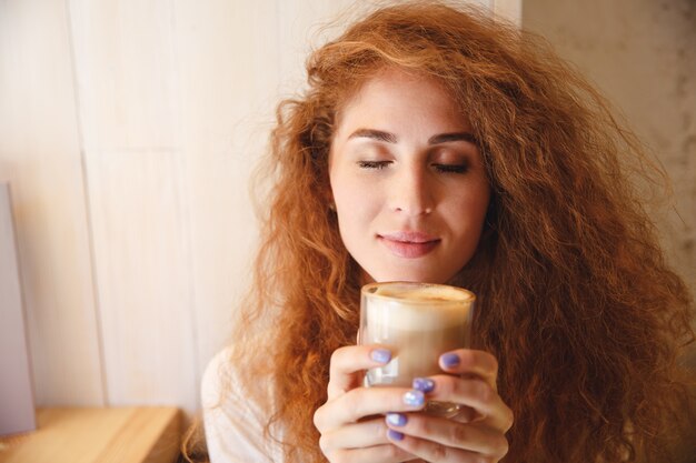 Retrato de una mujer bastante joven que huele su bebida de café