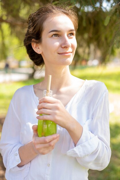 Retrato de mujer bebiendo jugo de botella de vidrio mirando a otro lado