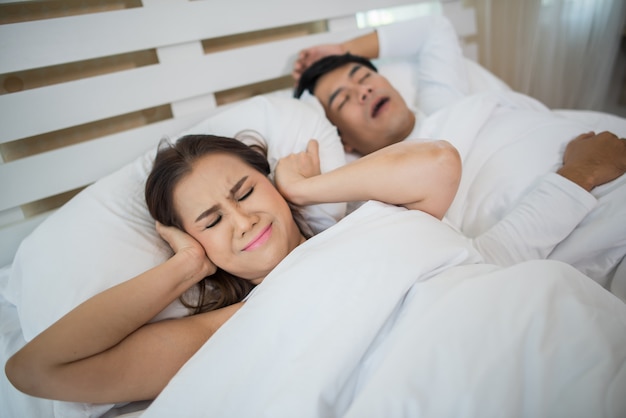 Retrato de mujer bloqueando orejas con hombre durmiendo ronquidos en cama