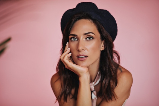 Retrato de mujer con boina mirando a cámara sobre fondo rosa. Hermosa chica con ojos grandes con pelo corto y corto posando en aislados.