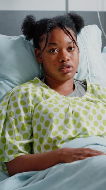 Retrato de mujer con bolsa de goteo intravenoso en la cama de la sala de hospital. Paciente joven con enfermedad que se prepara para recibir tratamiento sanitario y medicamentos contra la enfermedad. Persona enferma mirando a la cámara