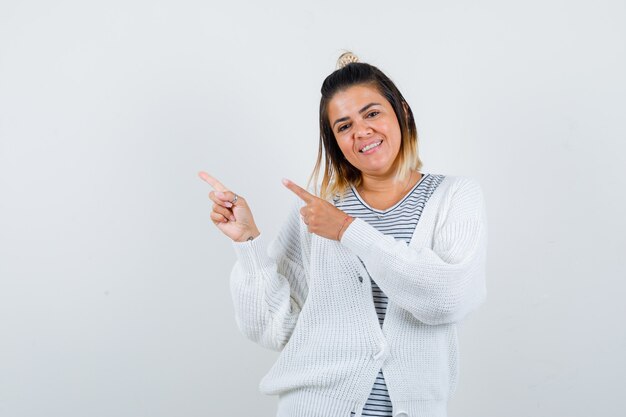 Retrato de mujer bonita apuntando a la esquina superior izquierda en camiseta, cárdigan y mirando alegre