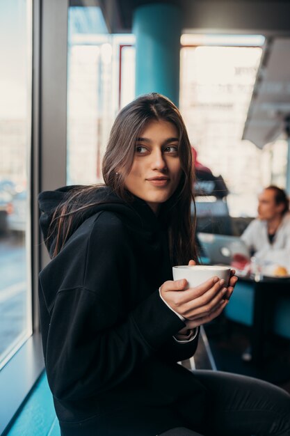 Retrato de mujer bonita bebiendo café de cerca. Señora sosteniendo una taza blanca con la mano.