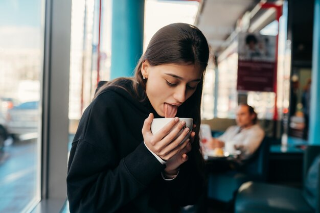 Retrato de mujer bonita bebiendo café de cerca. Señora sosteniendo una taza blanca con la mano.